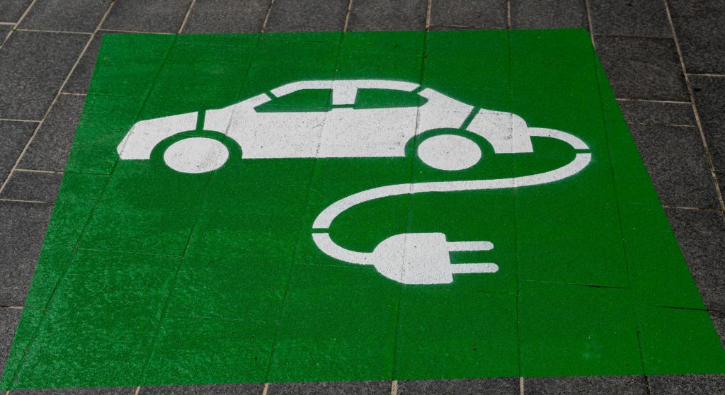 Guide d’achat : comment choisir sa voiture électrique en 2025 ? Un logo blanc sur fond vert pour marquer un emplacement de charge de véhicule électrique.