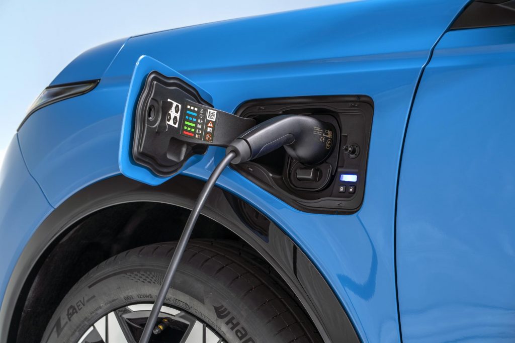 detailed shot of open electric charging port with a charger plugged in on left side above the wheels